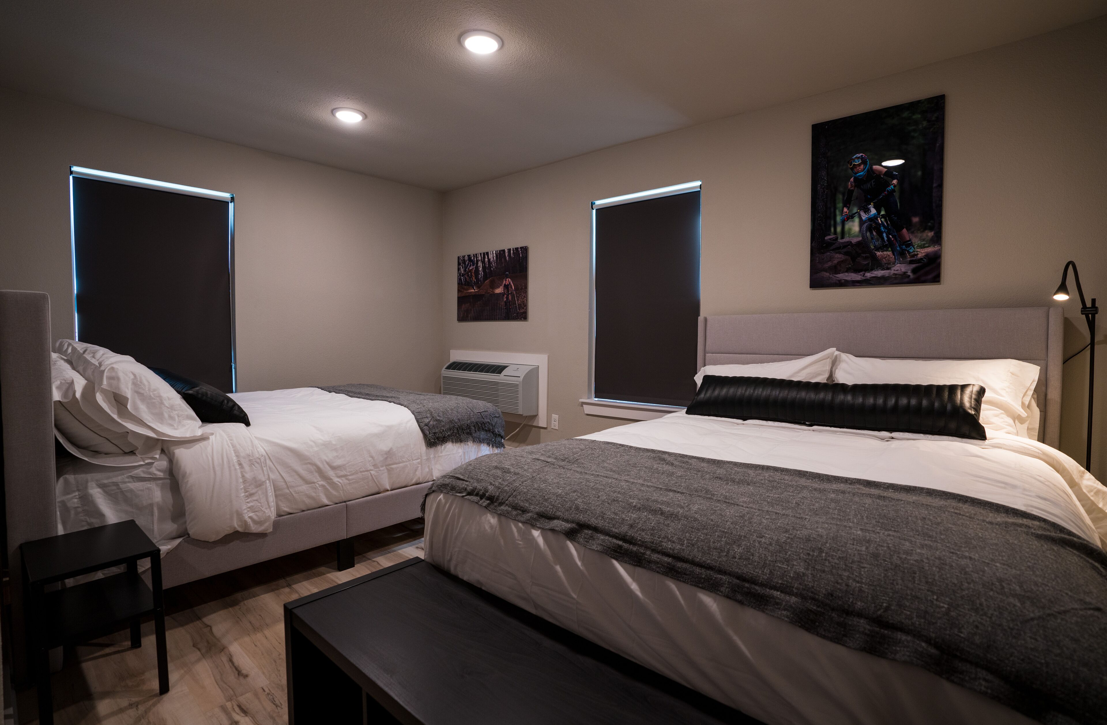 Un dormitorio moderno con dos camas, un banco y aire acondicionado instalado.