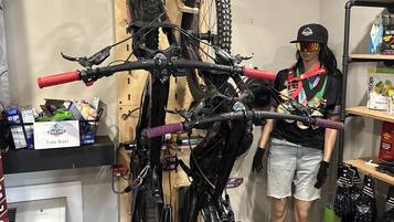 Une pièce dans laquelle on peut voir un vélo fixé sur un support en bois, un mannequin vêtu d’une tenue de cycliste, et divers accessoires de cyclisme disposés sur des étagères.