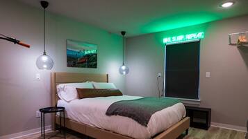 Un dormitorio con cama, dos lámparas colgantes, un televisor montado en la pared y un letrero de neón.