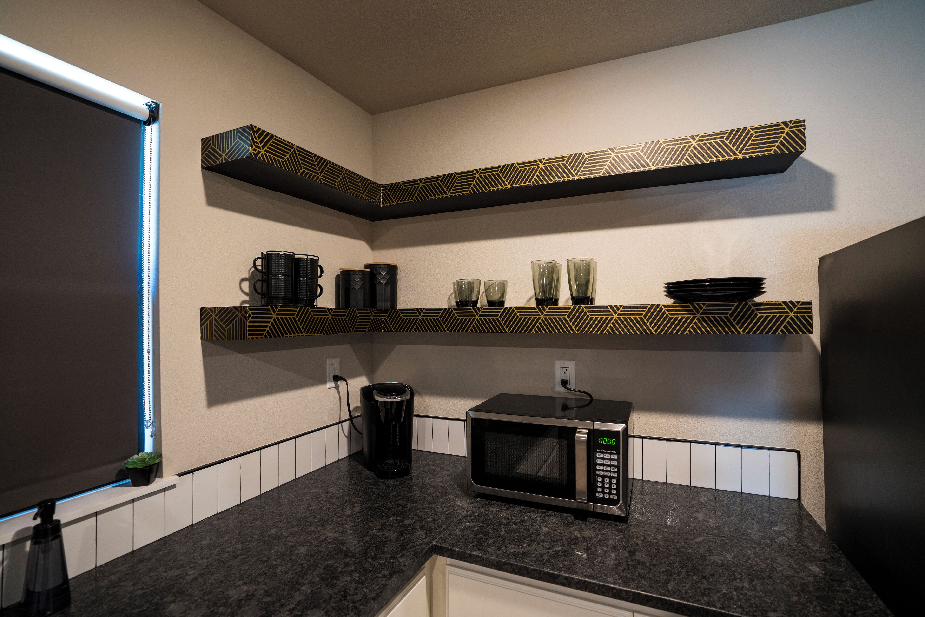 A kitchen with a microwave, coffee maker, and shelves with cups and plates.
