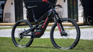 A mountain bike with a red handlebar and black frame, parked on grass in front of a building with two doorways. - The Bike Inn (Bentonville)