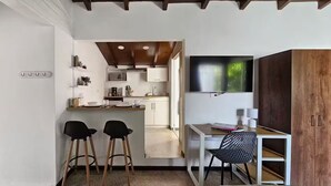 A compact kitchen with white cabinets, a microwave, and a wooden ceiling. There are two black chairs and a white table with a black chair. A wooden wardrobe is on the right.