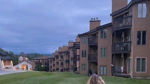 A residential area with multi-story buildings, a grassy lawn, and a clear sky. - Ski in/out @Base Lodge at  Clock tower,Okemo. Building B  Ground Level sleeps 6 (Ludlow)