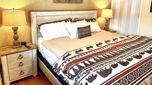 A neatly made bed with a patterned blanket, two bedside lamps, a nightstand with a clock, and a wall-mounted picture. - Ski in/out @Base Lodge at  Clock tower,Okemo. Building B  Ground Level sleeps 6 (Ludlow)