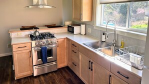 Una cocina moderna con estufa de acero inoxidable, microondas y fregadero. Se aprecia una ventana con vista a espacios verdes.