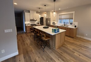 A modern kitchen with wooden cabinets, a central island with bar stools, pendant lighting, and a built-in oven. - Lodge House (Arlington)