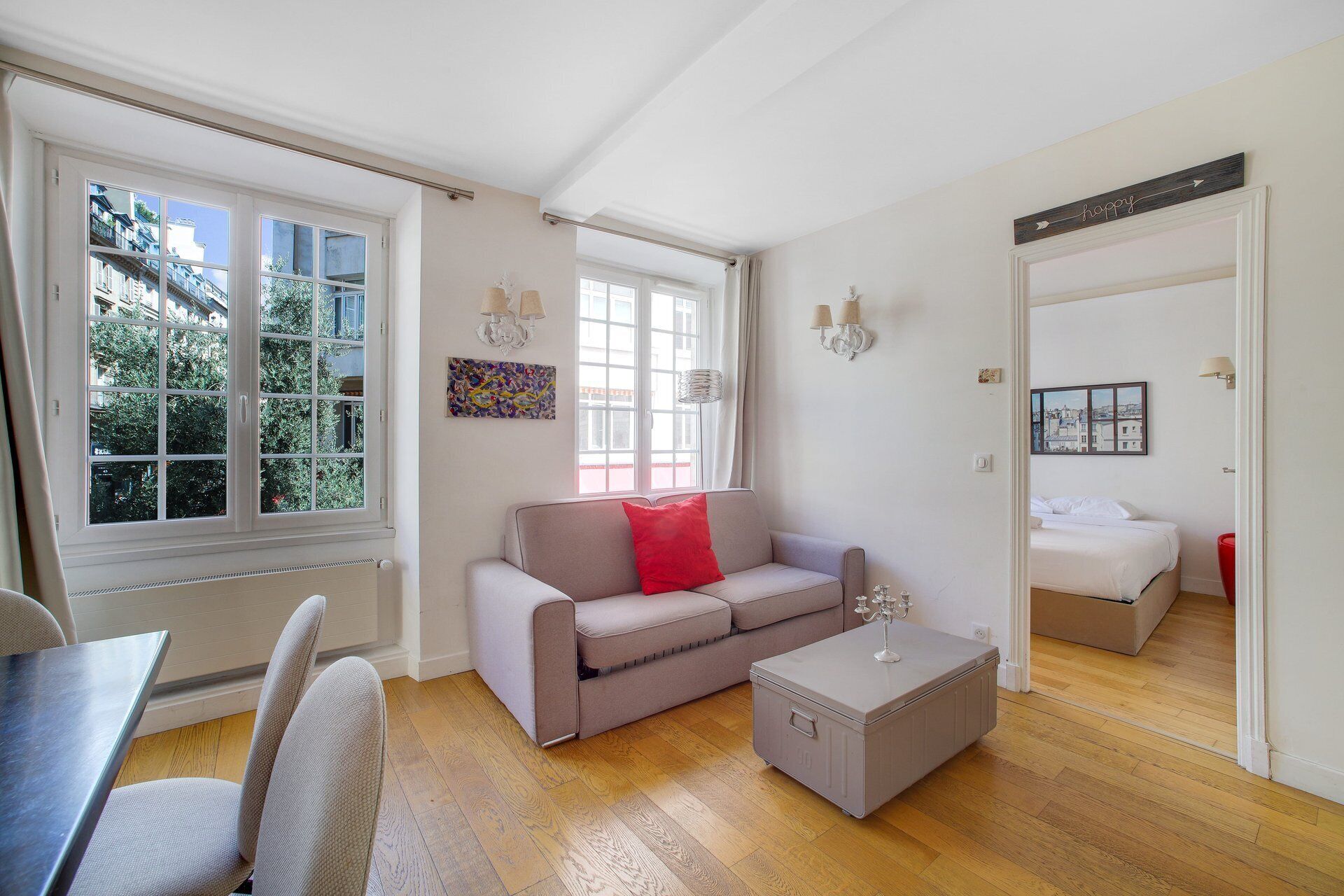 Ein modernes Wohnzimmer mit einer Couch, einem Couchtisch, einem Esstisch mit Stühlen, einem Bett und Blick auf Gebäude durch große Fenster.
