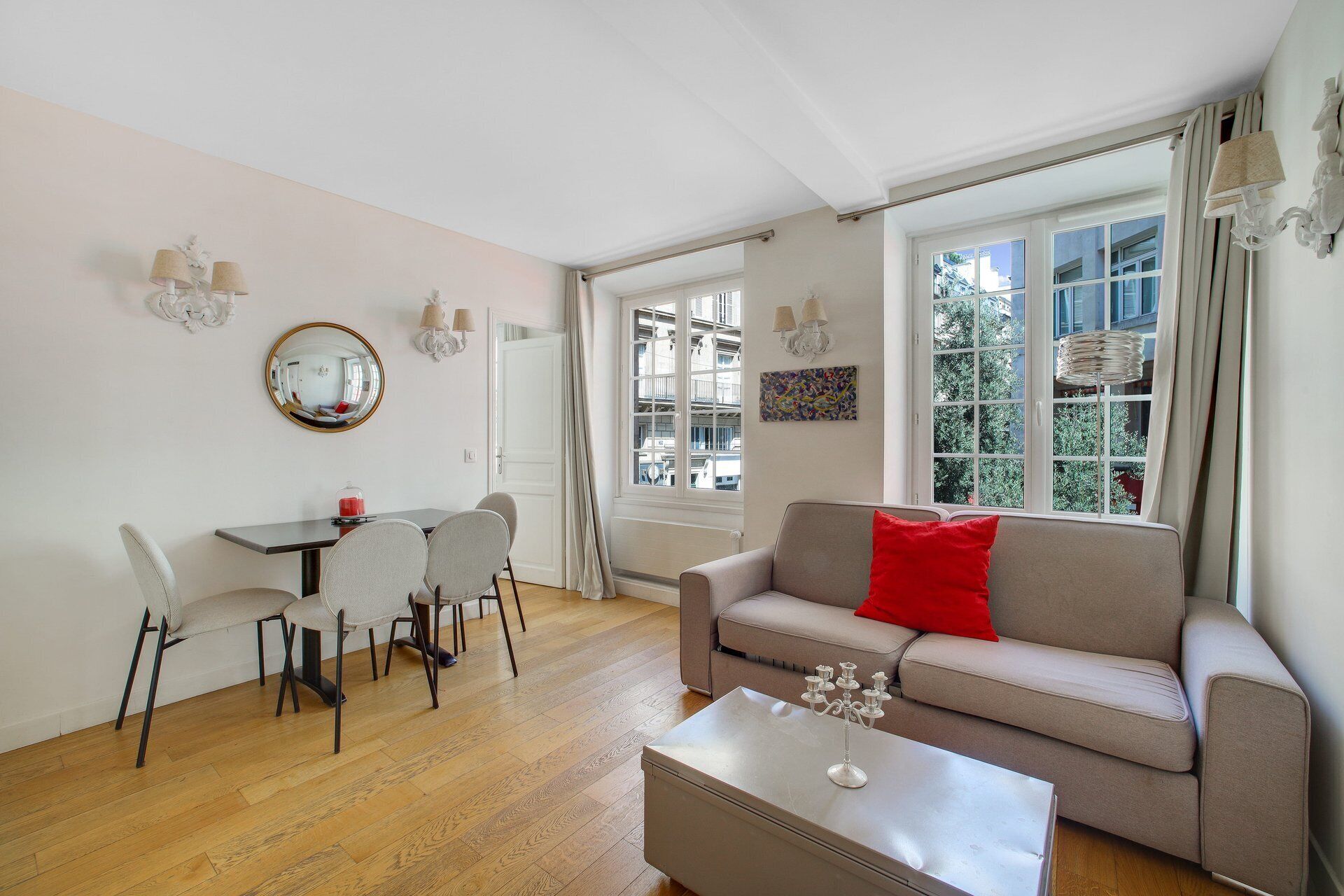 A living room with a sofa, a dining table with chairs, a coffee table, a mirror, and a window with curtains.