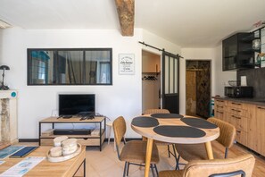 Een eetruimte met een ronde tafel, stoelen, een televisie en een keuken met kastjes en een magnetron.