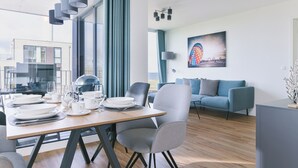 Un comedor moderno con una mesa de madera dispuesta para cuatro personas, sillas grises y vistas de la ciudad a través de amplias ventanas.
