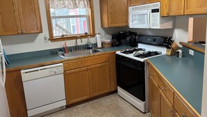 A kitchen with wooden cabinets, a stainless steel sink, a white dishwasher, a black stove, and a microwave. - Anchored At Last 3-bed Condo Kill Devil Hills w/ Large Deck and View of the Pool (Kill Devil Hills)