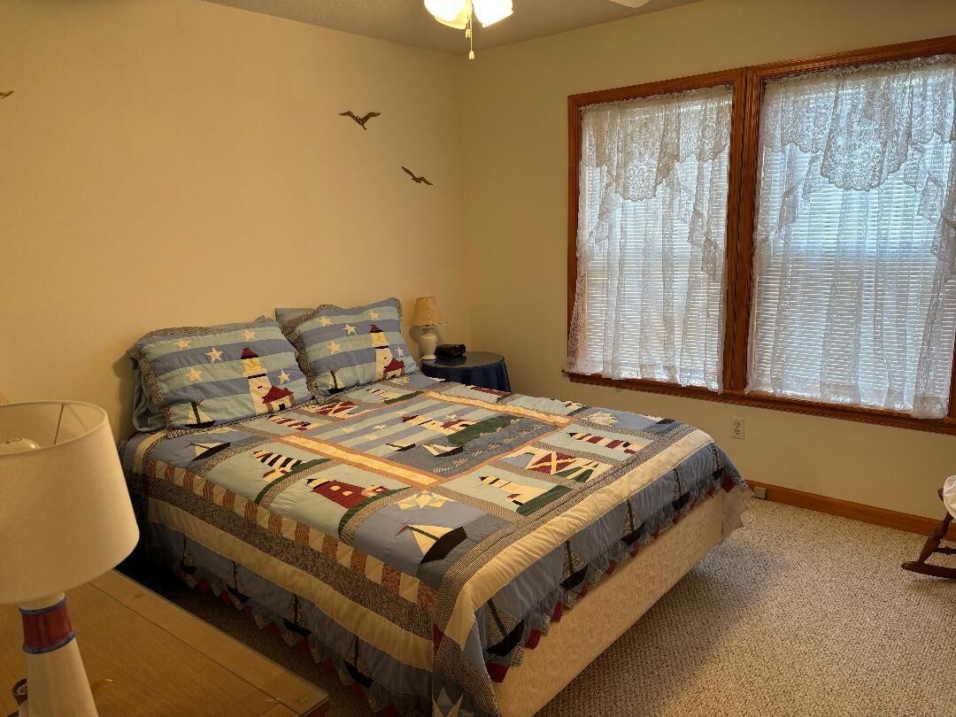 Une chambre à coucher avec un grand lit, une table de chevet, une lampe et une fenêtre avec des rideaux.