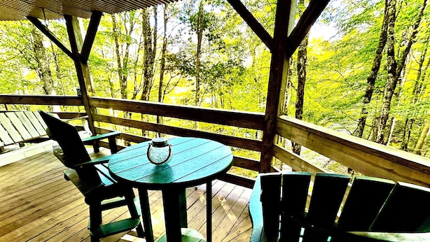 A wooden deck with a table and chairs, overlooking a forest. - Sugar's Edge Luxury Mountain Treehouse with AirCon (Sugar Mountain)