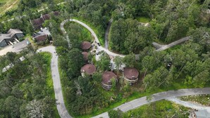 An aerial view of a residential area with winding roads, surrounded by dense greenery and several buildings with dome-shaped roofs. - Sugar's Edge Luxury Mountain Treehouse with AirCon (Sugar Mountain)