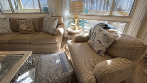 A cozy living room with a beige sofa, patterned cushions, and a view of a forest through large windows. - Sugar's Edge Luxury Mountain Treehouse with AirCon (Sugar Mountain)