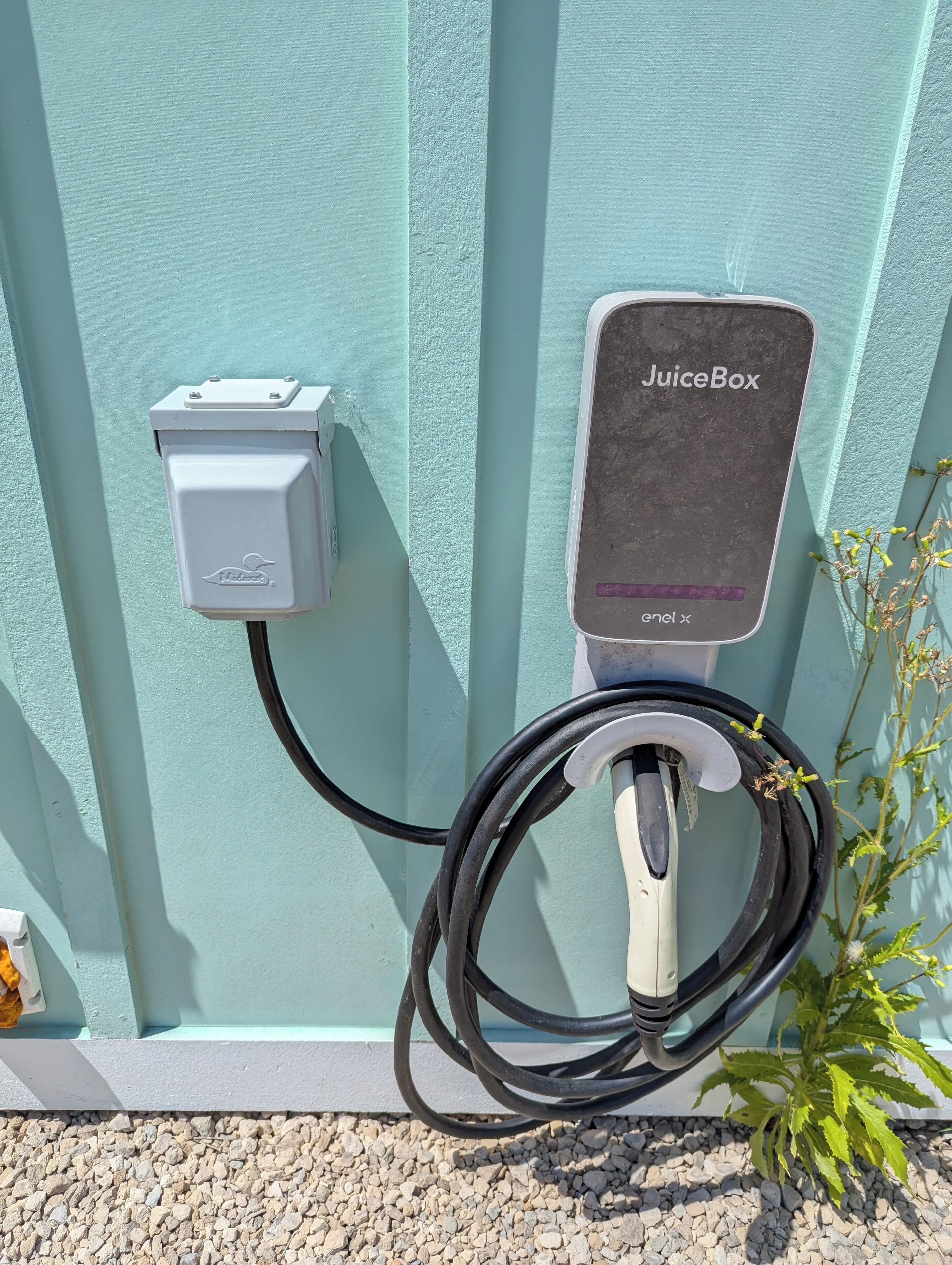 An electric vehicle charging station with a JuiceBox charger, a cable, and a small box with a logo.