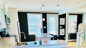 A modern kitchen with a central island, two grey upholstered chairs, and a round glass table. - Cozy, Relaxing, Center City Retreat with Private Rooftop Deck! (St. John's)