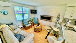 A modern living room with a sofa, two armchairs, a coffee table, and a TV. There is a fireplace and a kitchen area with a sink and countertop. - Cozy, Relaxing, Center City Retreat with Private Rooftop Deck! (St. John's)
