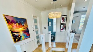 A staircase with wooden steps and white railings, leading to a landing with a chandelier. - Cozy, Relaxing, Center City Retreat with Private Rooftop Deck! (St. John's)