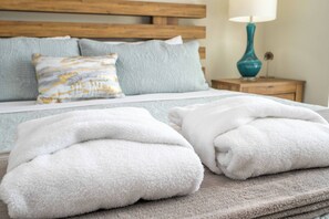 A neatly made bed with white towels, a wooden headboard, and a nightstand with a lamp.