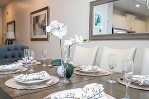 A dining table set with white plates, silverware, and clear glasses, surrounded by white chairs.