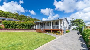 A modern two-story house with a covered porch, solar panels, and a well-maintained lawn. - The Sussex Beach Bach (Sussex Inlet)
