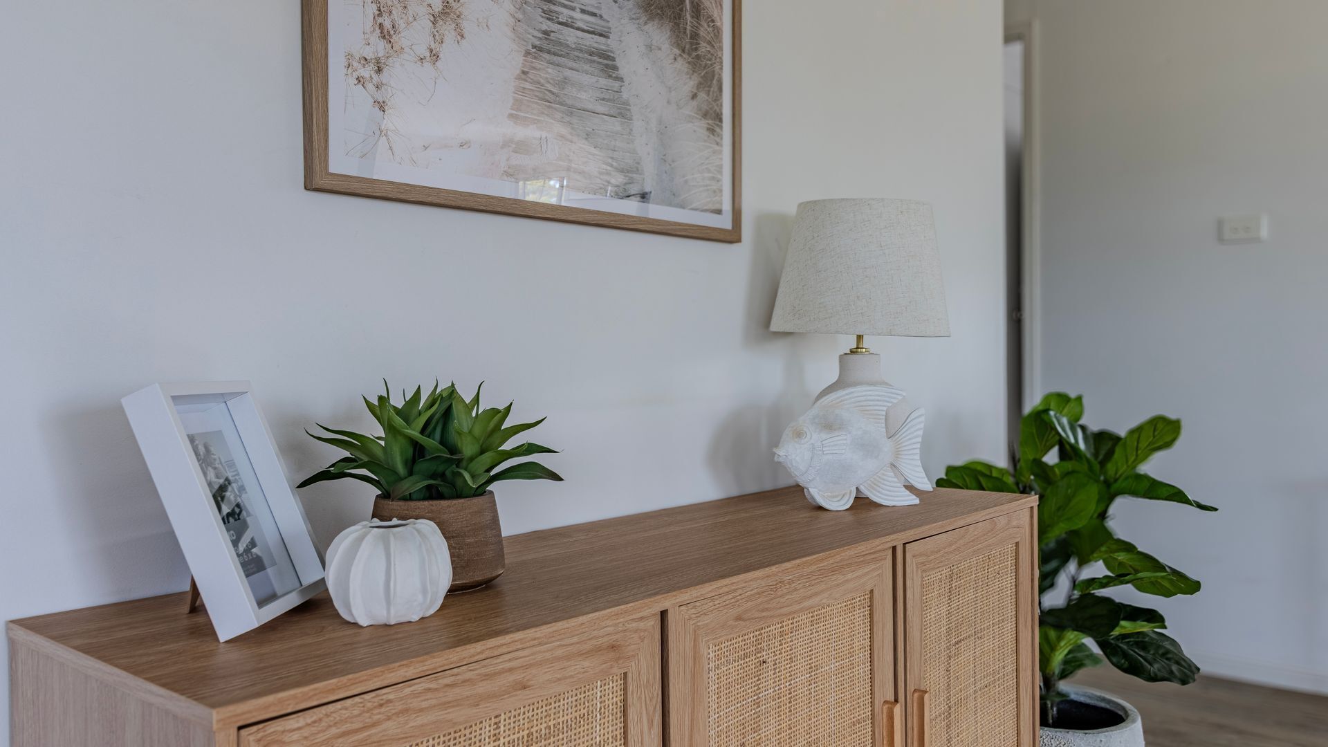 A wooden console table with a framed photo, a potted plant, a lamp, and a fish-shaped lamp base.