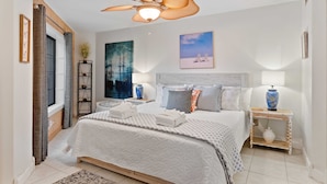 A bedroom with a large bed, a ceiling fan, a nightstand with a lamp, and artwork on the walls. - Beach, Indoor and Outdoor Pools, Hot tub, Tennis walk Coligny Plaza! (Hilton Head Island)