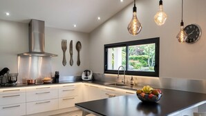 Una cocina moderna con armarios blancos, una campana de acero inoxidable y un amplio ventanal con vistas a zonas verdes.