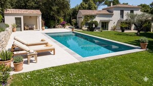 Un área junto a la piscina con sillones de descanso, un edificio pequeño y una casa con tejado de tejas.