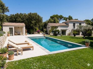 A poolside area with lounge chairs, a small building, and a house with a tiled roof. - das Haus des Paradieses (Saint-Restitut)