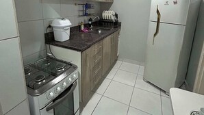A compact kitchen with a gas stove, oven, white refrigerator, and wooden cabinets.
