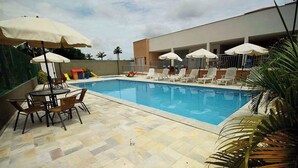 A swimming pool with lounge chairs and umbrellas, surrounded by a tiled patio area.