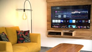 Ein modernes Wohnzimmer mit einem gelben Sofa, einem Holztisch und einem an der Wand befestigten Fernseher, der eine Streaming-Dienstanwendung zeigt.