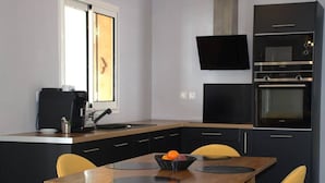 Eine moderne Küche mit einem Holzesstisch und gelben Stühlen, einer schwarzen Arbeitsplatte und einem eingebauten Backofen.