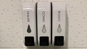 En väggmonterad tvåldispenser med tre fack märkta med "HÅR", "BALSAM" och "KROPP".