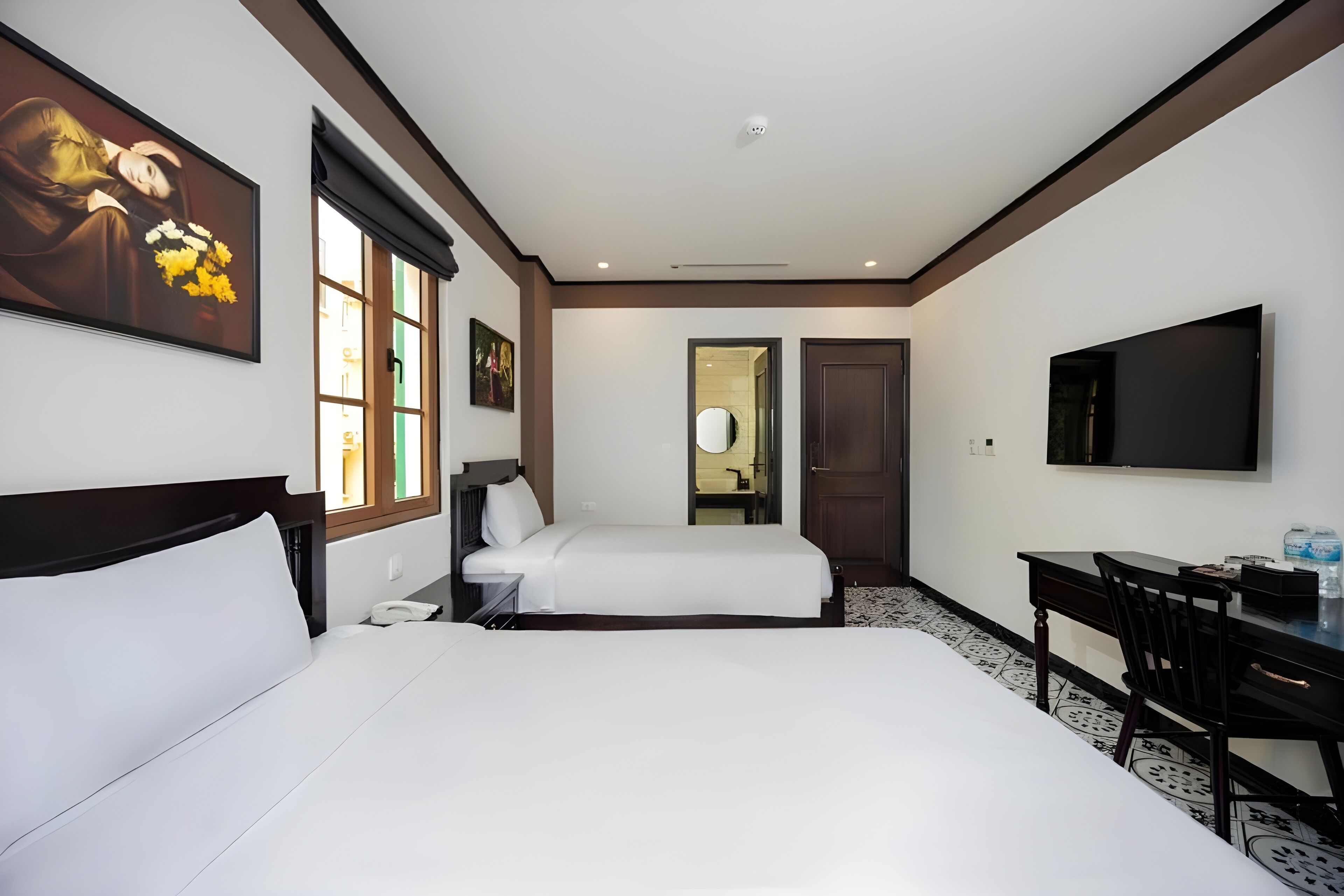 A hotel room with two beds, a desk, a chair, a TV, and artwork on the walls.