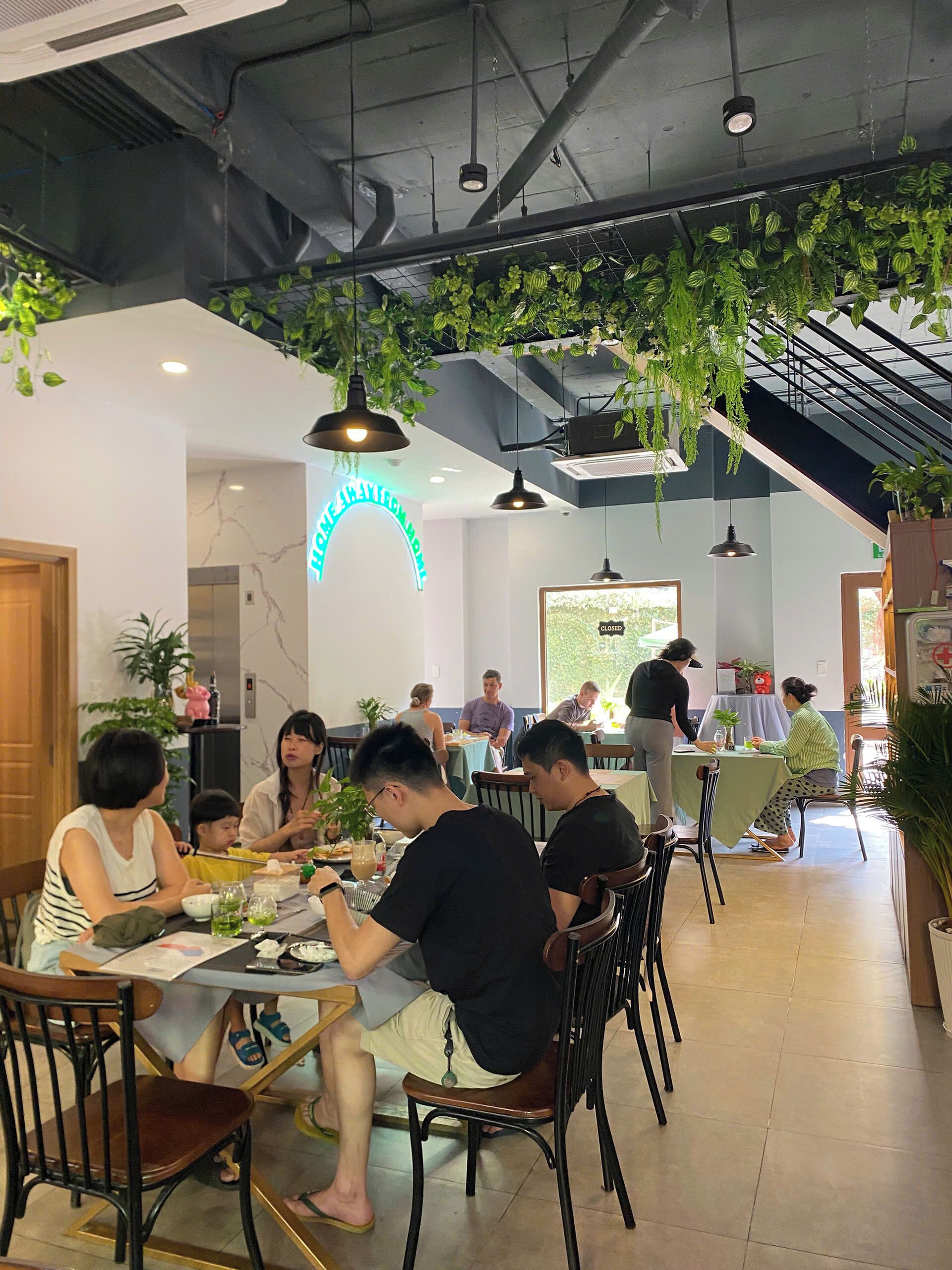 A restaurant with indoor plants, hanging lights, and a neon sign.