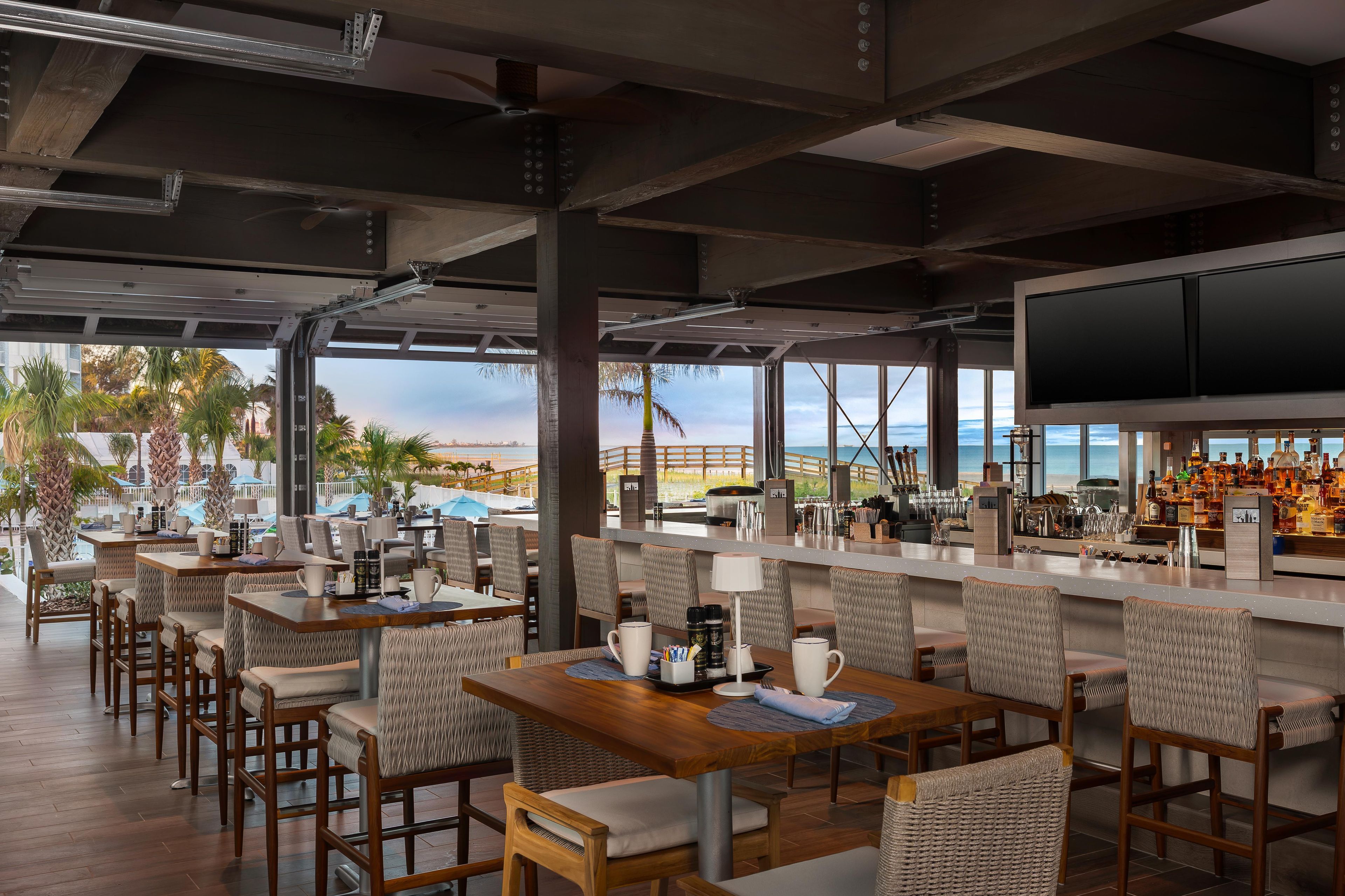 An outdoor bar area with seating, a television screen, and a view of the sea.