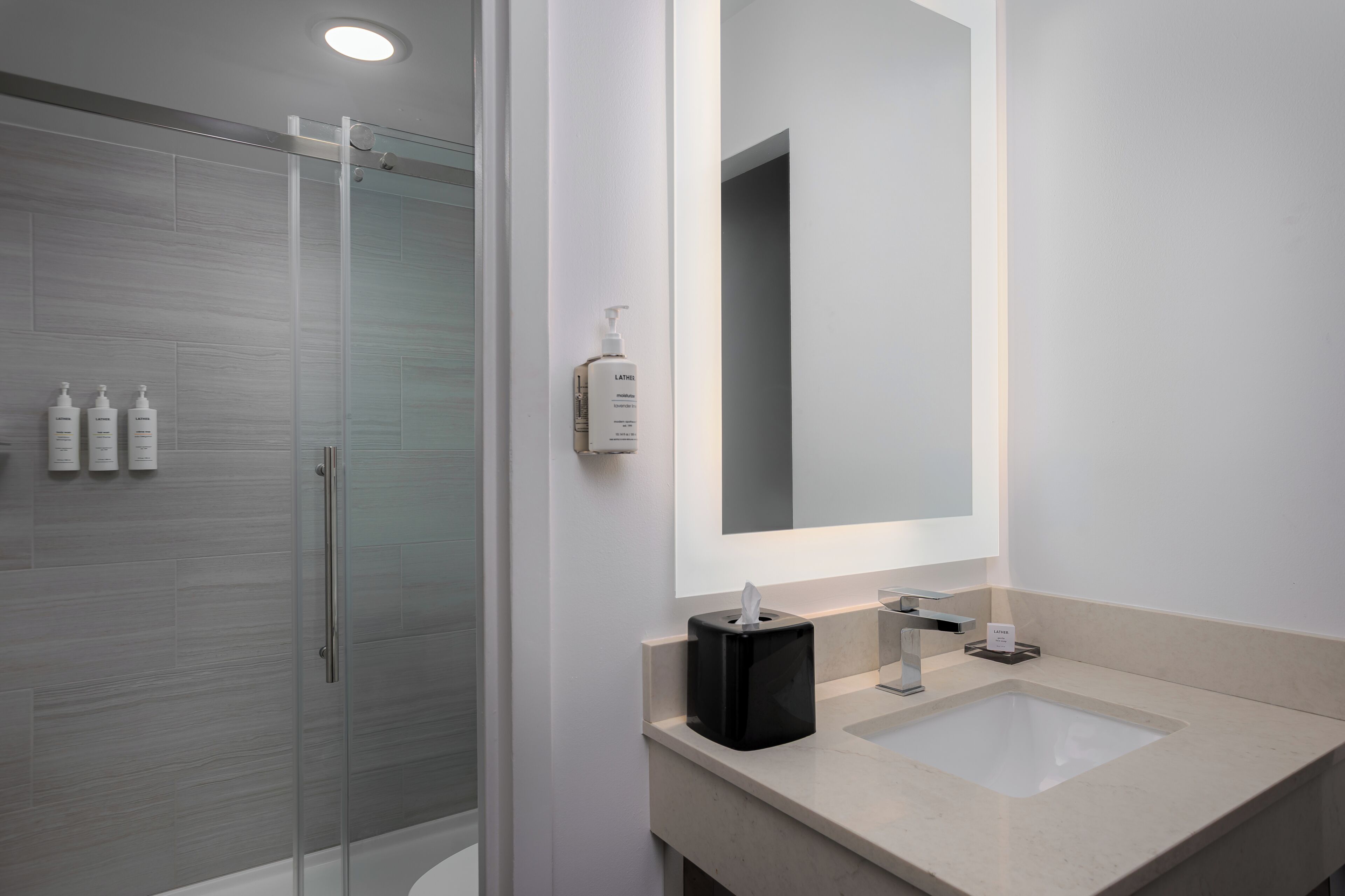 A modern bathroom with a glass shower enclosure, a large mirror, and two sinks.