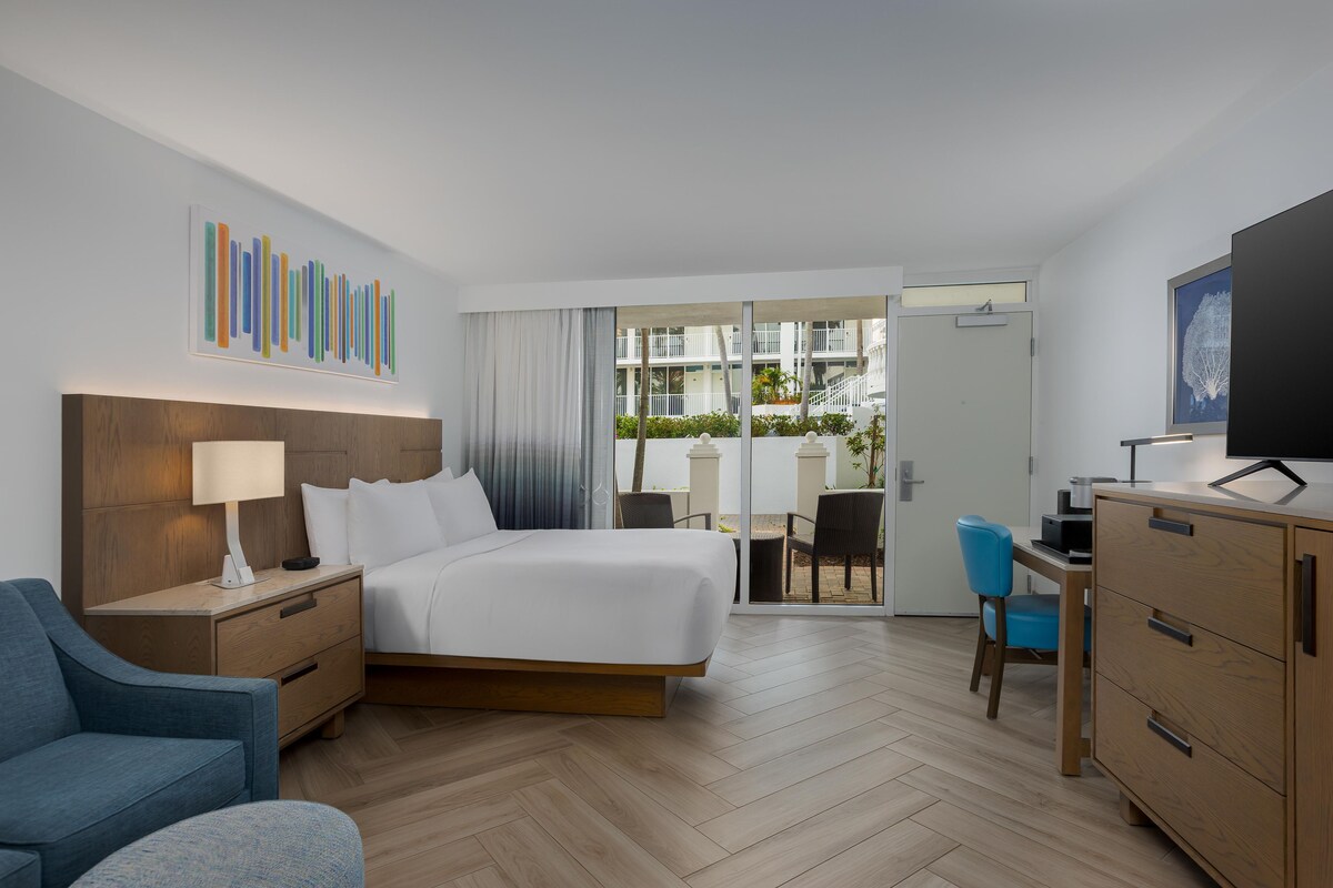 Habitación de hotel con cama, escritorio, silla, televisor y vista al exterior.