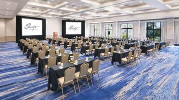 A conference room with rows of tables and chairs, large windows, and a blue carpet.