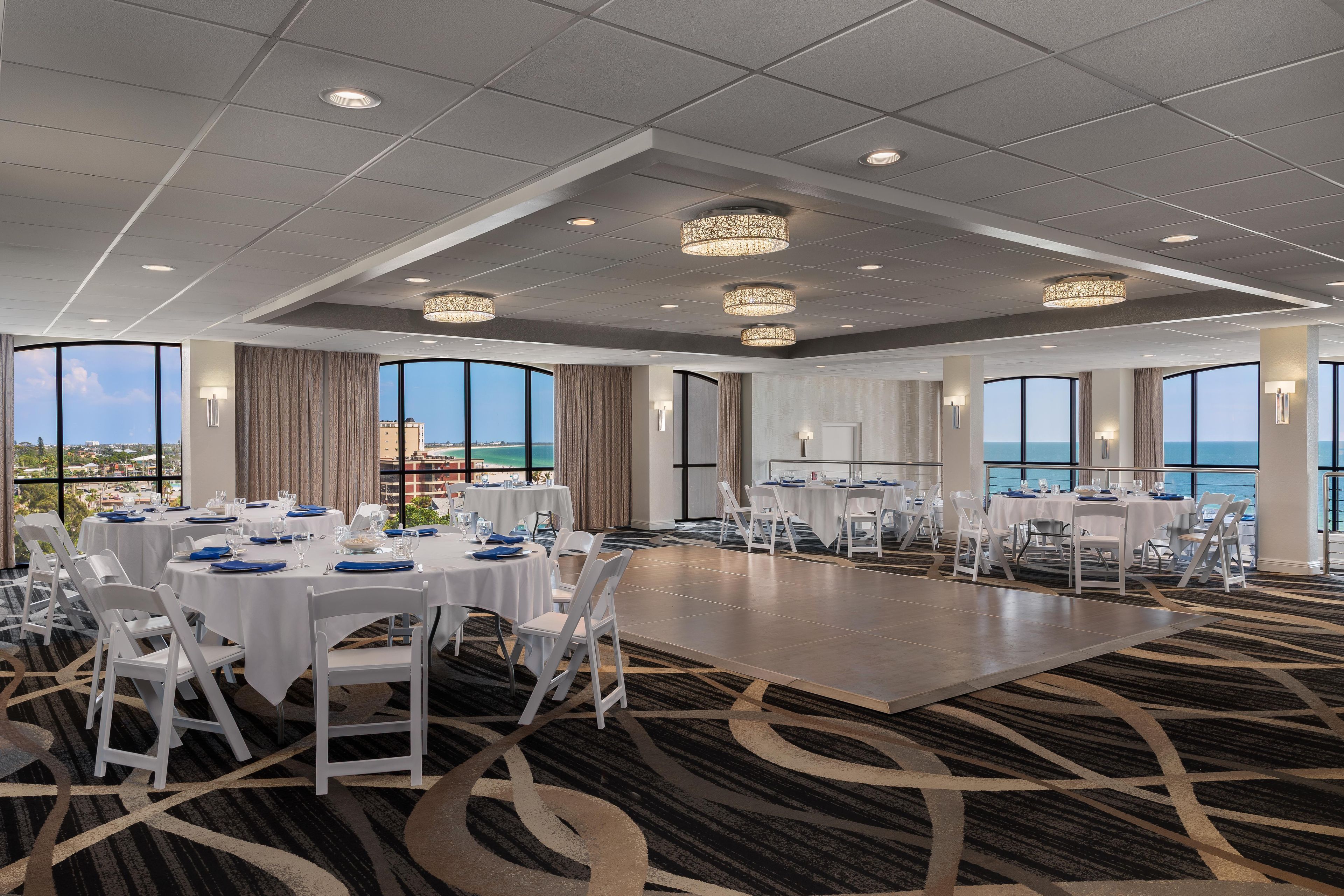A conference room with round tables, white chairs, and large windows offering a view of the ocean.