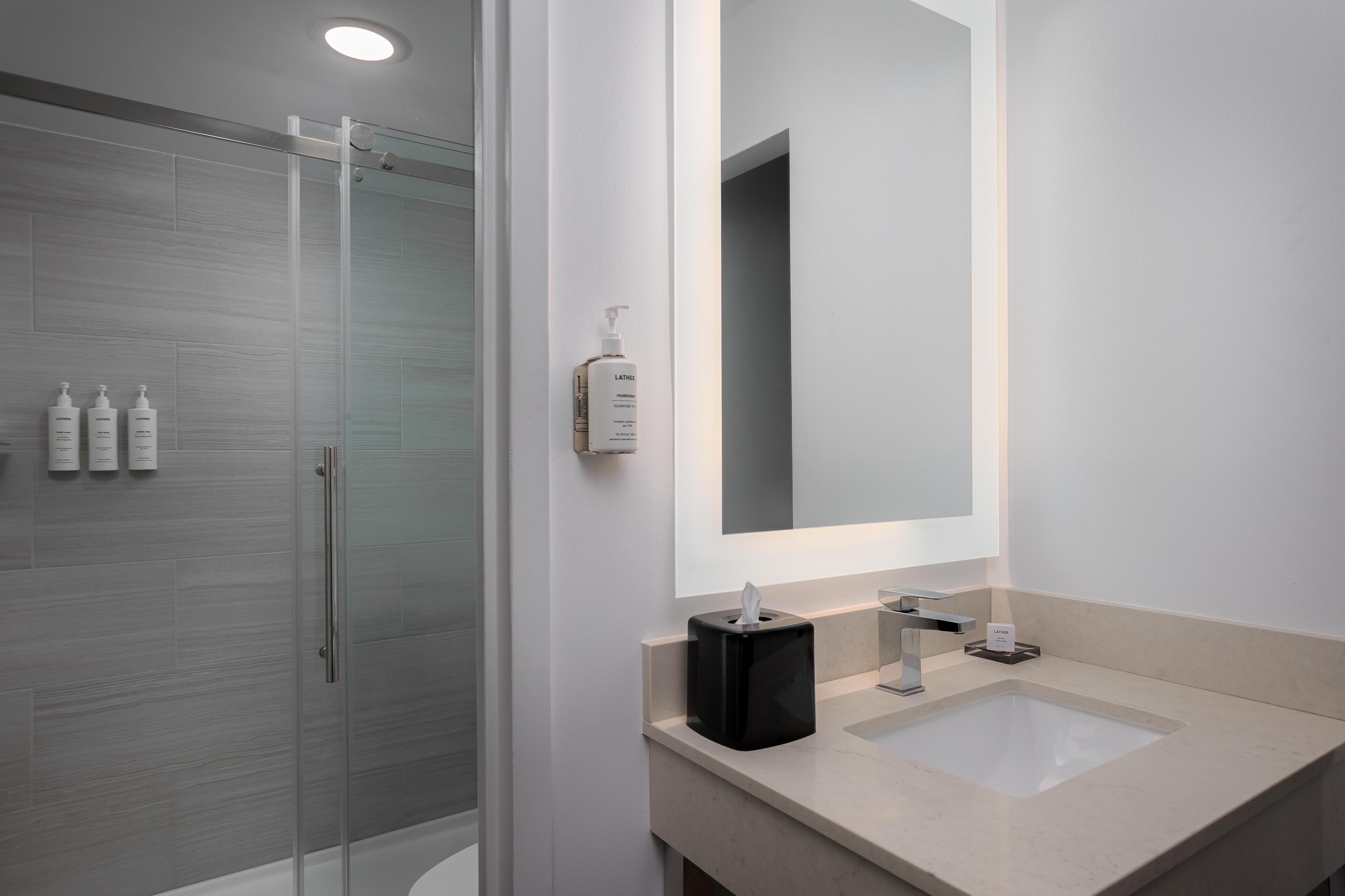 Un baño moderno con cabina de ducha de vidrio, un espejo grande y una encimera color beige.