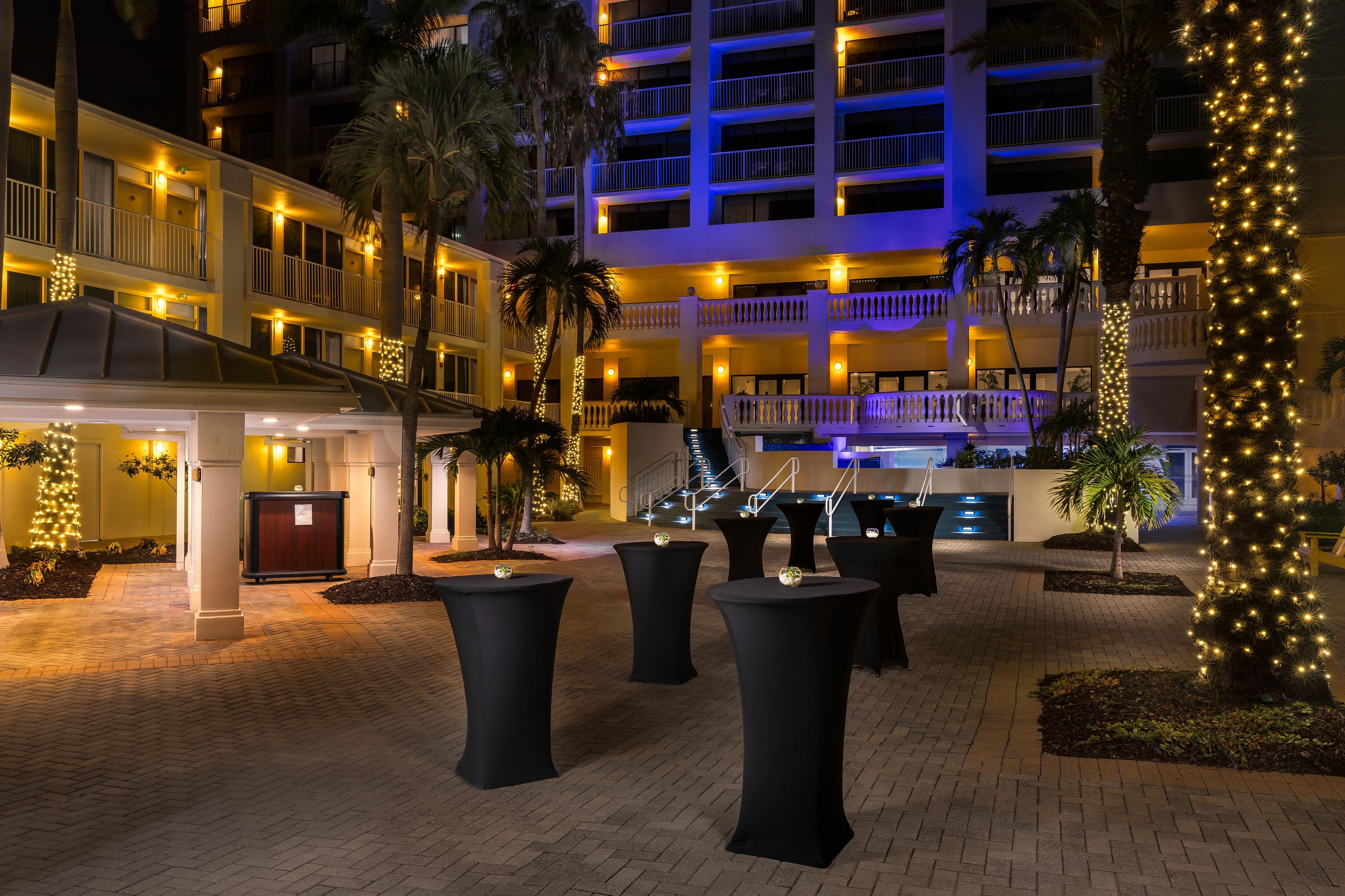 A hotel courtyard at night with outdoor seating, palm trees, and illuminated balconies.