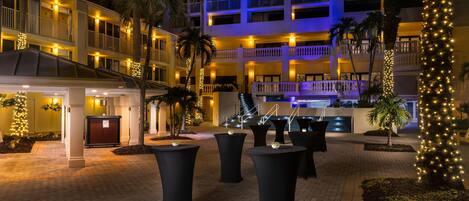 A hotel courtyard at night with outdoor seating, palm trees, and illuminated balconies.