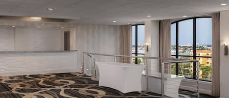 A hotel room with a large window, a bed, a desk, and a patterned carpet.