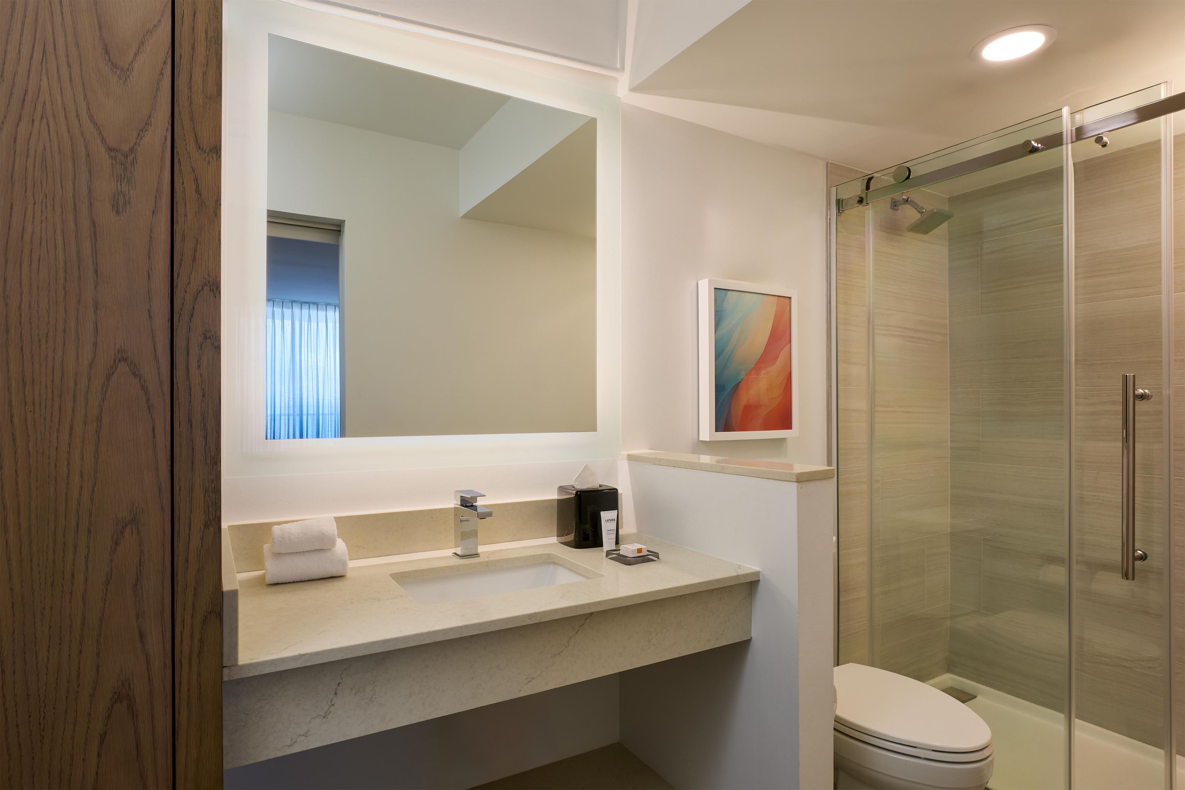 A bathroom with a large mirror, a sink, a toilet, and a shower area.