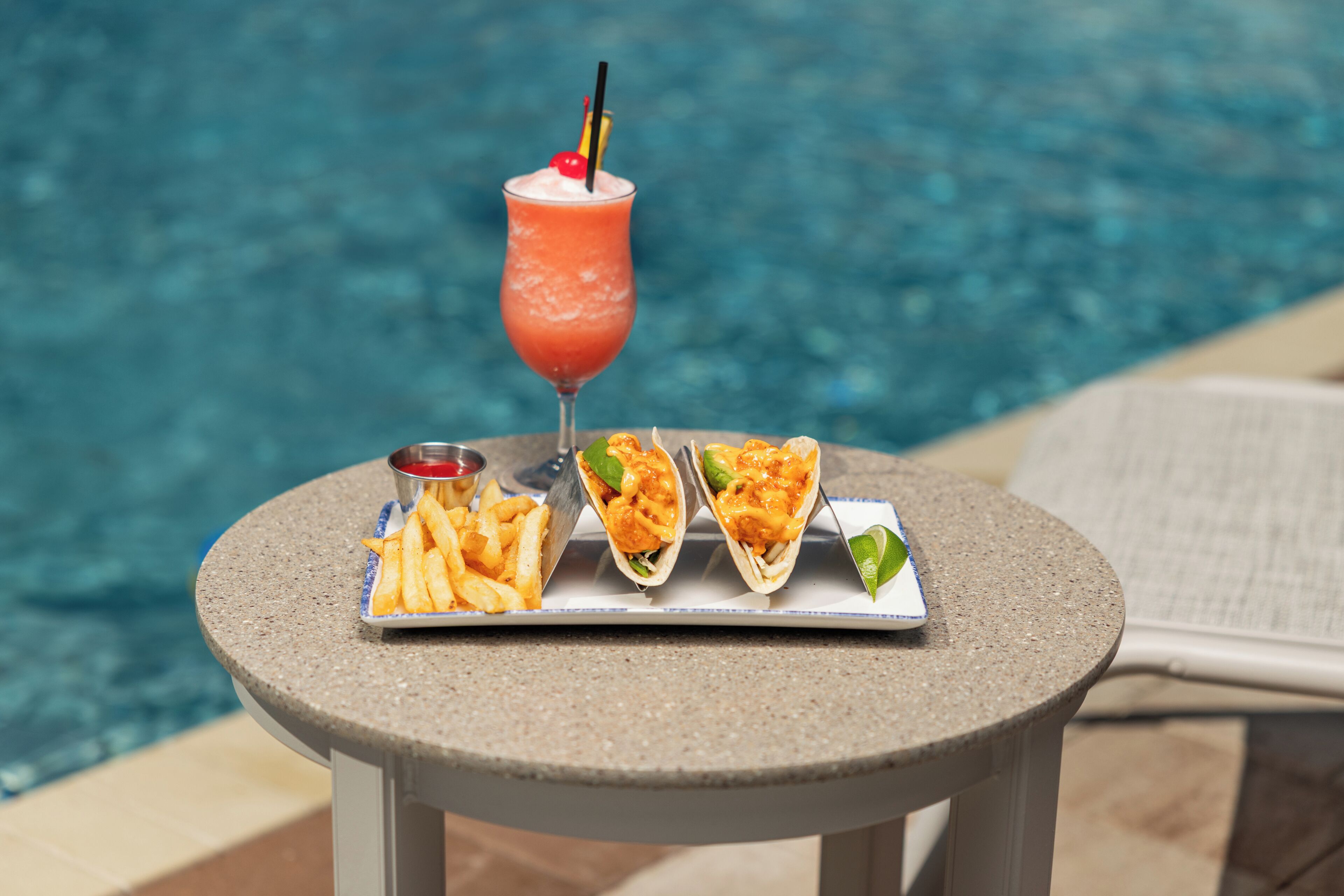 A table with a drink, fries, and tacos by a pool.