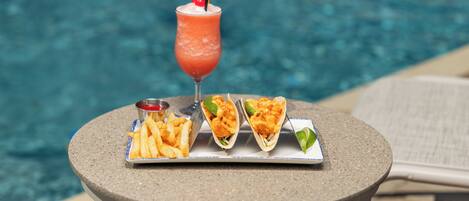 A table with a drink, fries, and tacos by a pool.